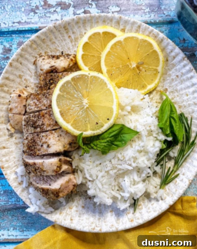 A beautifully plated baked lemon pepper chicken breast served with fluffy white rice, fresh lemon slices, and a garnish of basil, showcasing a vibrant and appealing meal.