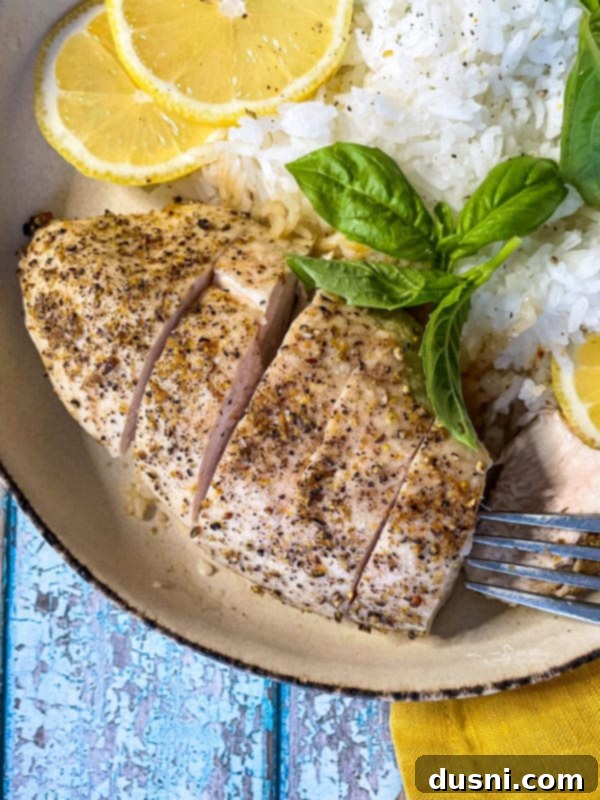 A serving of baked lemon pepper chicken, garnished with fresh lemon wedges and basil leaves, beside a bed of white rice, ready to be enjoyed.