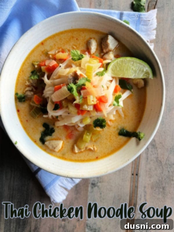 A close-up of a rustic white bowl filled with creamy Thai chicken noodle soup, ready to be enjoyed.