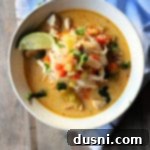 A bowl of Thai Chicken Noodle Soup, steaming and ready to eat, garnished with fresh cilantro and lime.