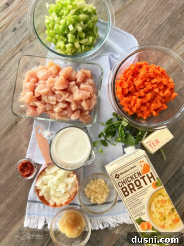 Array of fresh ingredients for Thai Chicken Noodle Soup: chicken, celery, carrots, chicken broth, garlic, ginger, cream, onions, red curry paste.
