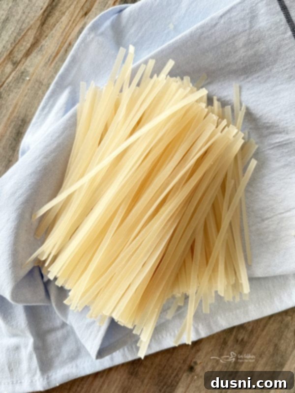 Uncooked rice noodles resting on a kitchen towel, ready to be prepared.