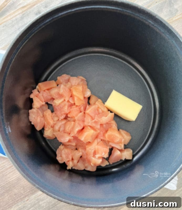 Diced chicken sautéing in melted butter in a Dutch oven, creating a fragrant base for the soup.