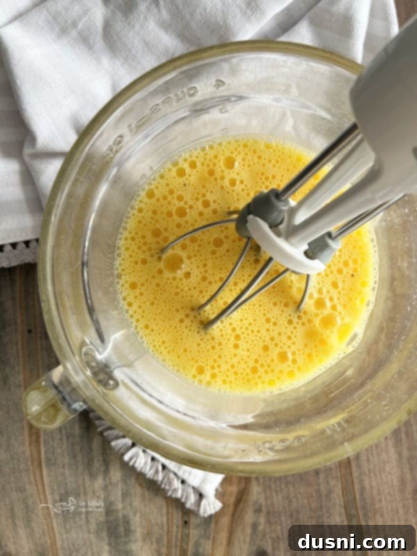 Egg Sliders Eggs being whisked thoroughly in a bowl with a mixer, preparing them for scrambling.