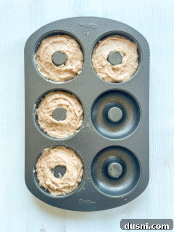 Close-up of donut batter being scooped into a donut pan, showing the golden texture of the batter.