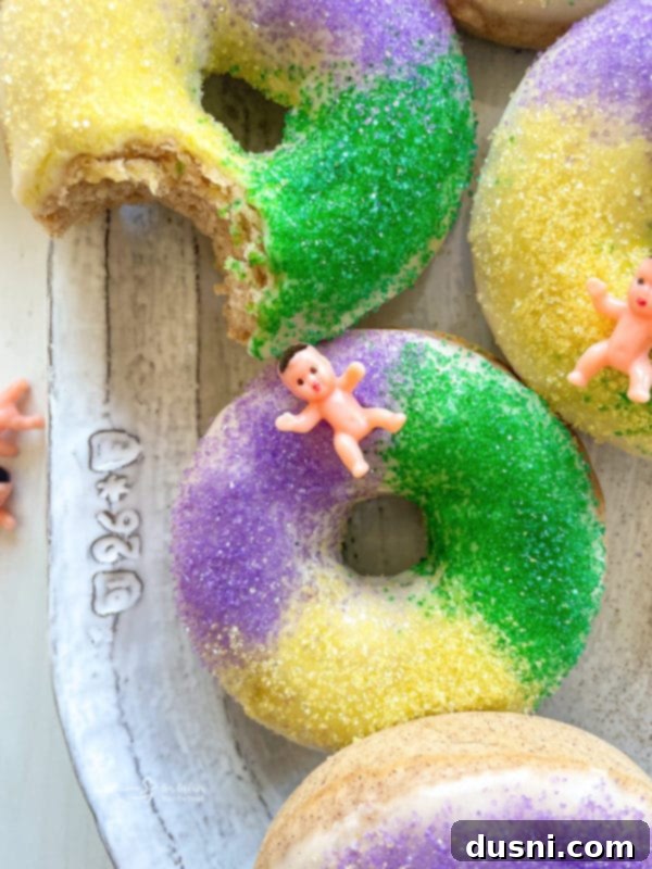 A hand dipping a King Cake donut into a bowl of sweet glaze, ready for decoration.