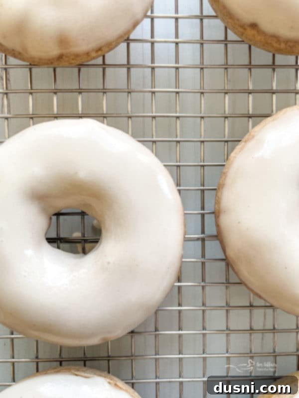 Three baked King Cake donuts on a white plate, one with a plastic baby, and purple, green, and gold sugar sprinkles.