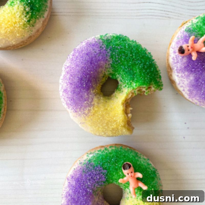 Several baked King Cake donuts arranged on a white background, showcasing their colorful sugar and glaze.
