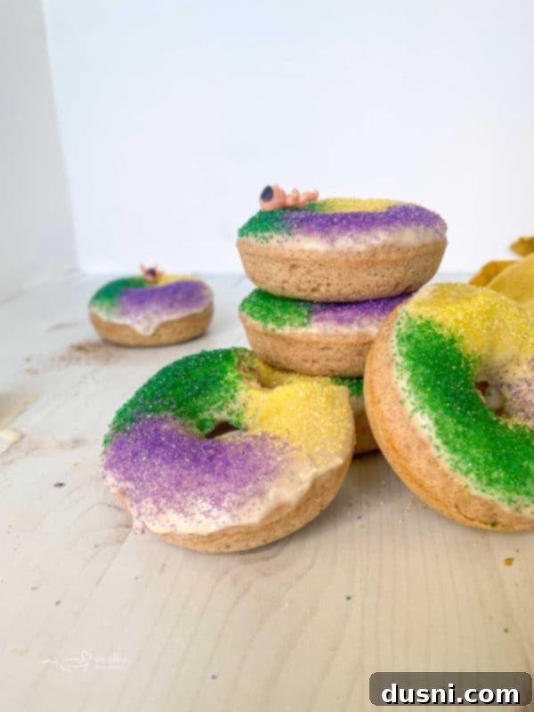 Two hands holding a baked King Cake donut covered in green, gold, and purple sparkling sugar.