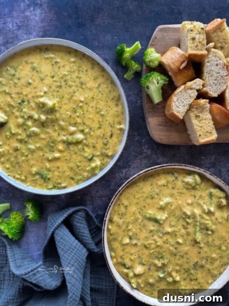 A close up of creamy broccoli cheese soup with visible broccoli florets and potato pieces.