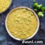 A white bowl with homemade broccoli cheese soup in it, garnished with fresh parsley.