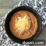 Unlock Restaurant Flavor in Canned Refried Beans 7 Overhead of Restaurant Style Refried Beans in a black bowl, garnished with cheese
