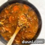 Hearty Beef and Mushroom Barley Soup 16 Stirring the Vegetable Beef Barley Soup with Mushrooms in the pot.