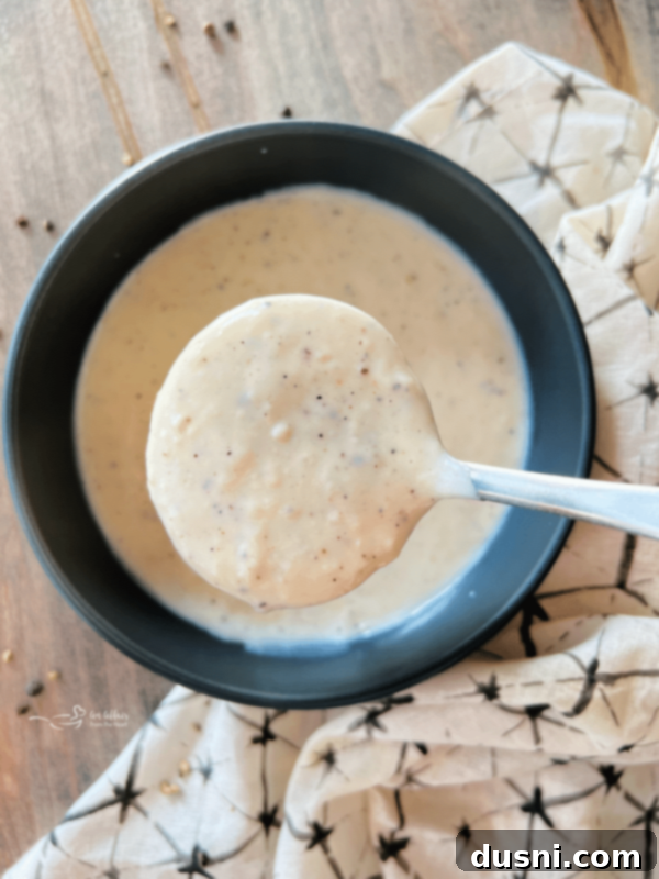 A bowl of creamy Homemade White Country Gravy with a spoon, ready to serve.