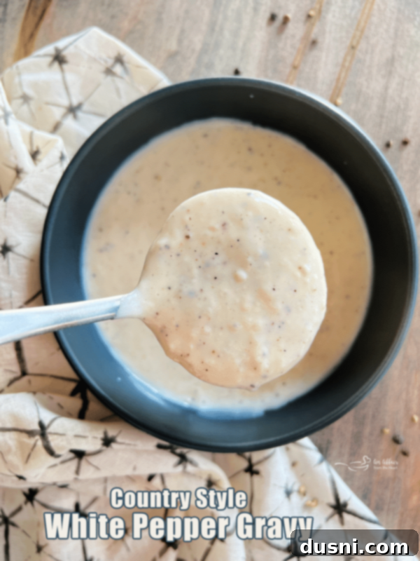 Homemade White Country Gravy in a bowl on a rustic wooden surface, with a spoon.