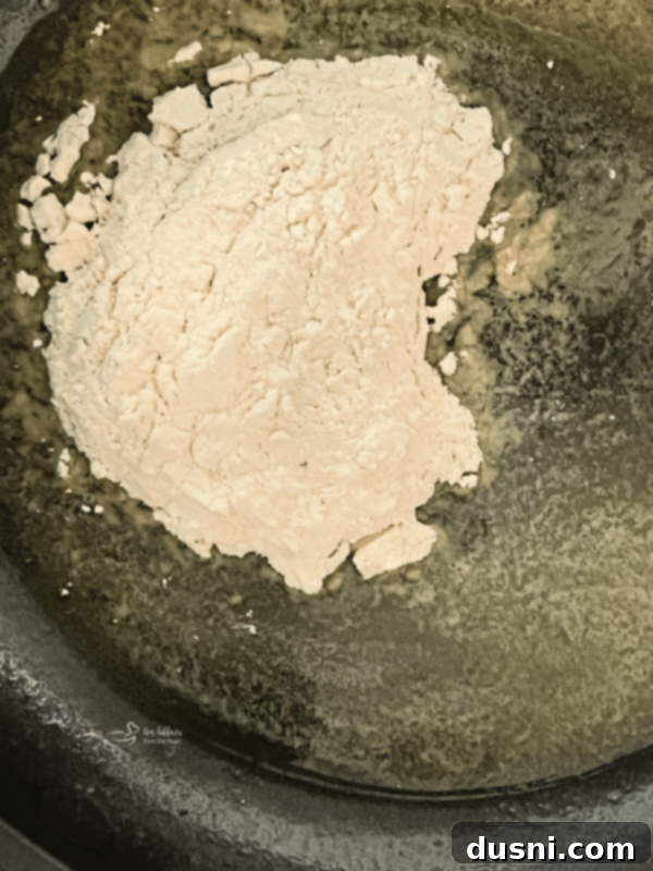 Flour being whisked into melted butter in a skillet to form a roux.