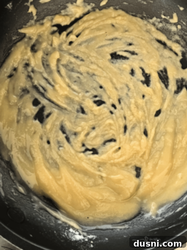 Roux cooking in a skillet, turning a light beige color, being stirred constantly.