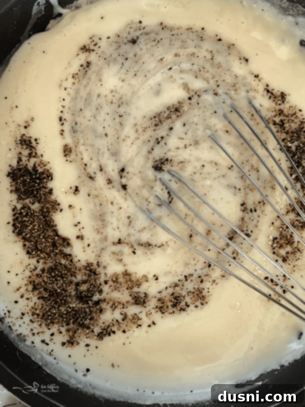 White gravy thickening in a skillet after milk has been added, being whisked.
