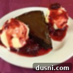 A slice of Flourless chocolate cake, and vanilla ice cream topped with a raspberry sauce all on a white plate
