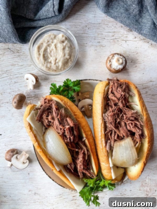 Mouthwatering Crock Pot French Dip Sandwiches 3 Two French onion French dip sandwiches, showcasing the shredded beef and melted cheese.
