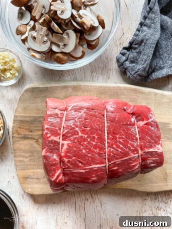 Mouthwatering Crock Pot French Dip Sandwiches 5 Top view of raw beef chuck roast on a wooden cutting board, prepped for slow cooking.