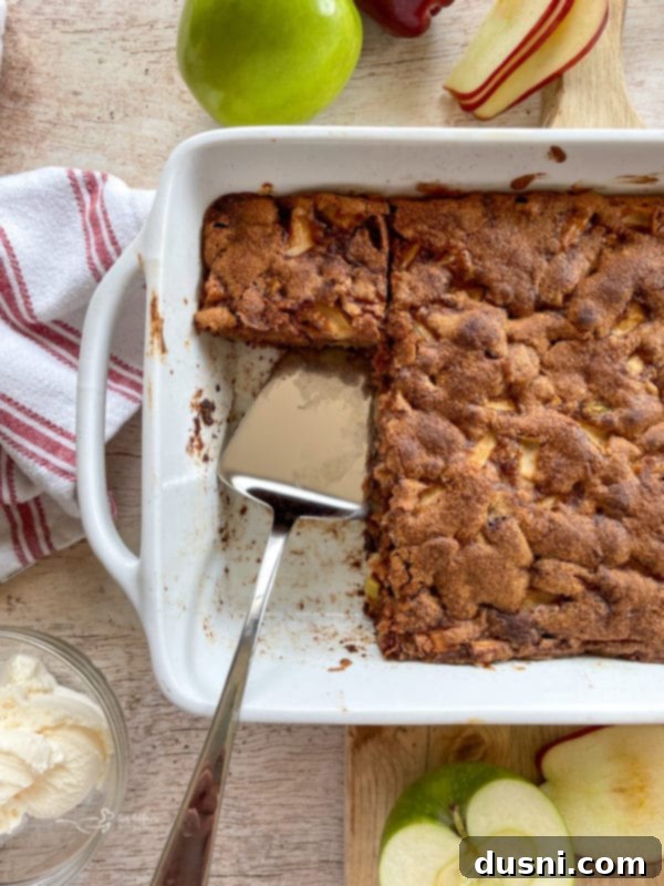 A perfectly cooked apple cake, golden brown and fragrant, cooling in its white baking pan after coming out of the oven.