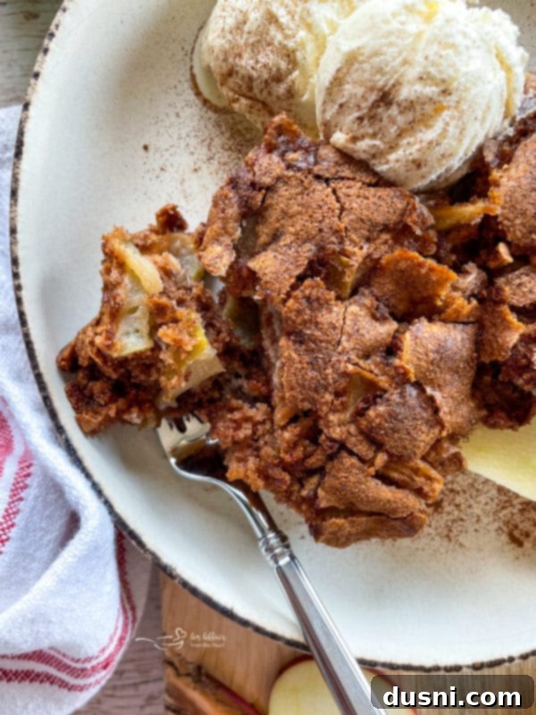 A tempting close-up of a slice of fresh apple cake with a fork, accompanied by a scoop of melting vanilla ice cream, ready to be eaten.