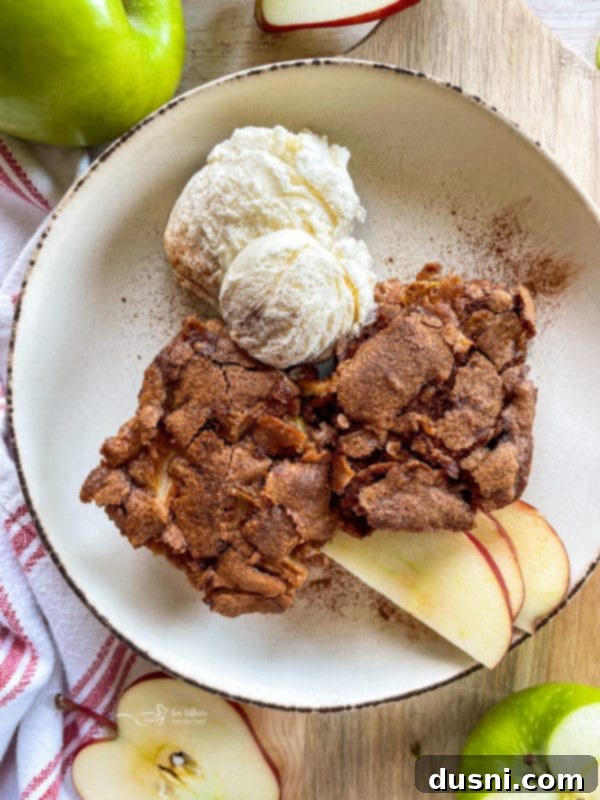 A close-up view of a slice of fresh apple cake, revealing its moist interior, studded with tender apple pieces, and served with a side of vanilla ice cream.