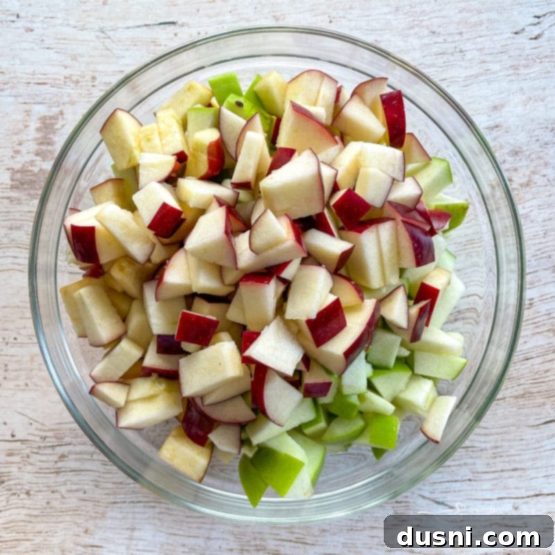 Close-up photo of uniformly diced fresh apples in a clear glass bowl, showcasing their readiness for the cake mixture.