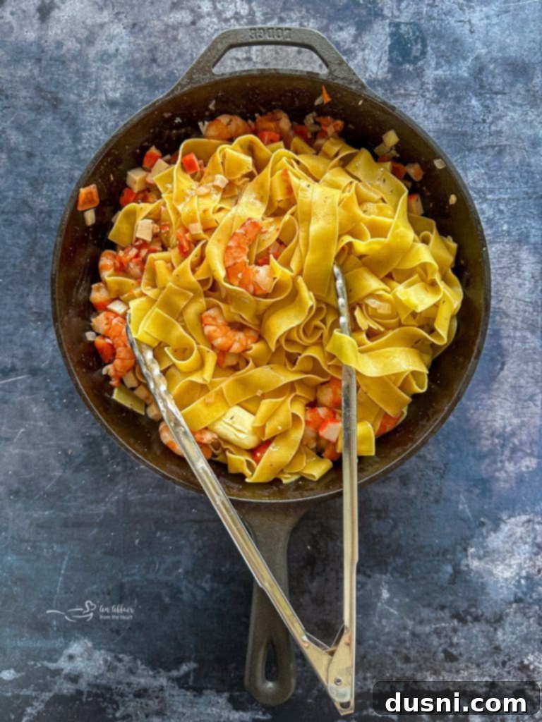 Coastal Crab & Shrimp Pasta 9 Diced tomatoes and crab meat being stirred into the shrimp and sauce in a skillet.