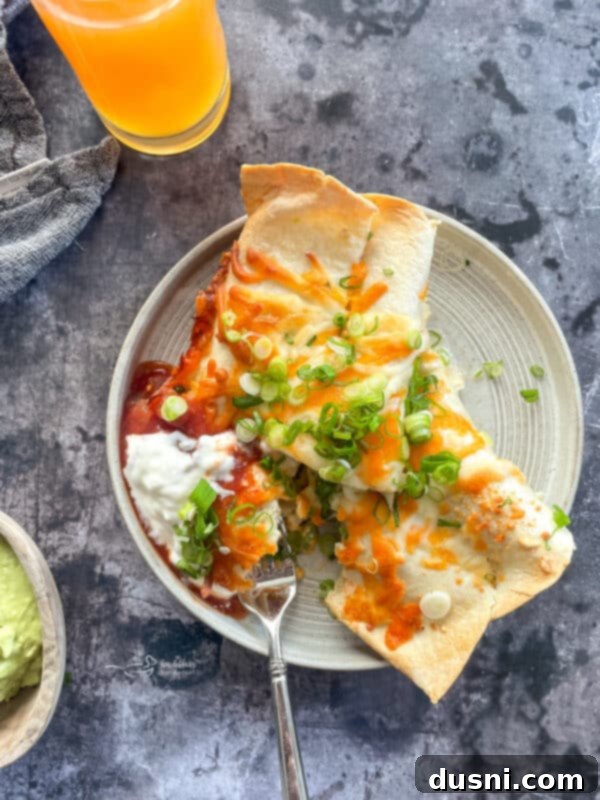 A serving of Brunch Enchiladas with Ham, garnished with salsa and sour cream, on a white plate