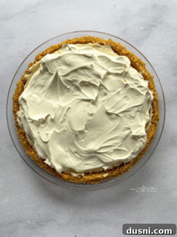 The remaining Cool Whip being spread over the peanut butter filling layer of the pie, creating a smooth white topping