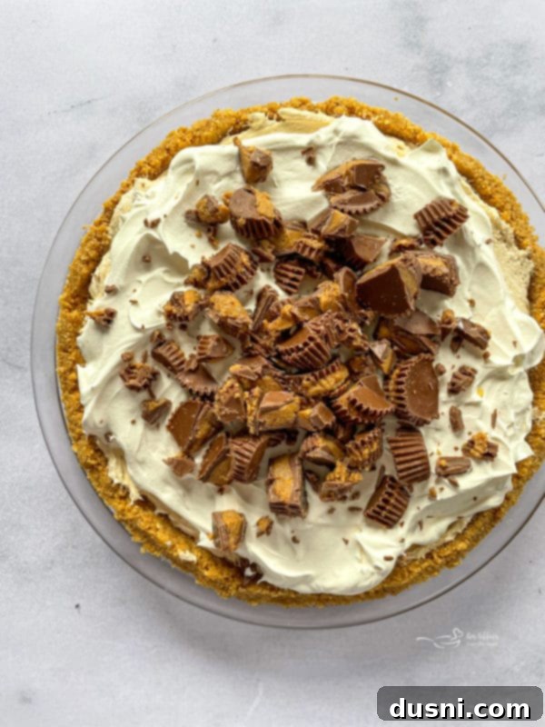 Chopped Reese's Peanut Butter Cups being sprinkled generously over the whipped topping of the no-bake pie