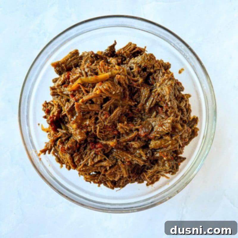 Tender Slow Cooker Pulled Beef Burritos 4 Cooked shredded beef in a slow cooker, ready for burritos, with some liquid remaining.