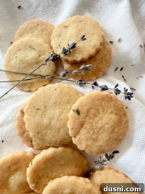 Lavender Shortbread and Lavender Strawberry Cream 2 A stack of heart-shaped lavender shortbread cookies, garnished with fresh lavender sprigs, on a light-colored background.