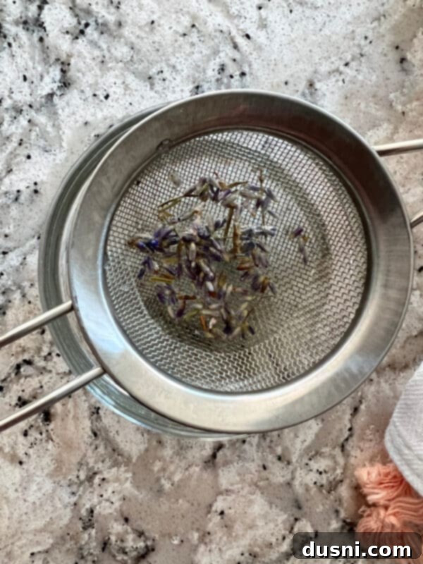 Lavender Shortbread and Lavender Strawberry Cream 20 Straining lavender syrup through a fine-mesh sieve to remove the dried lavender flowers, leaving a clear, fragrant liquid.