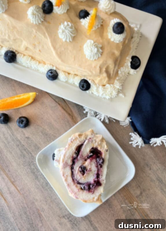 Blueberry Orange Cloud Roll 2 Beautifully garnished Blueberry Orange Angel Food Cake Roll slice on a plate.