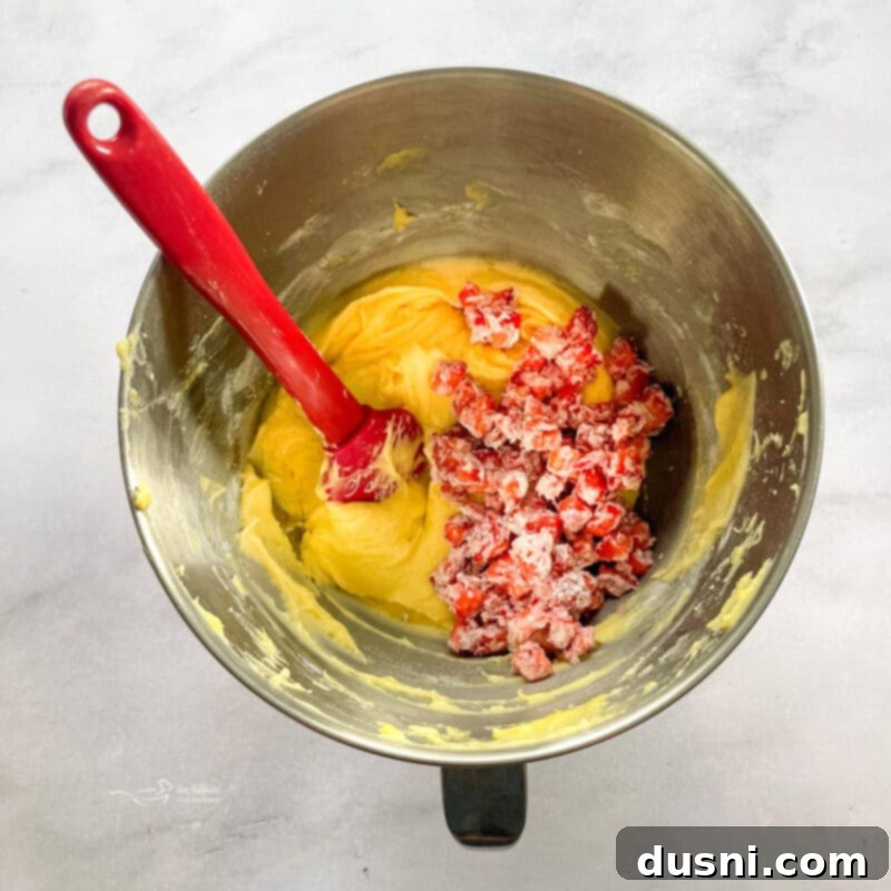 Folding flour-coated strawberries into strawberry bread batter with a rubber spatula.