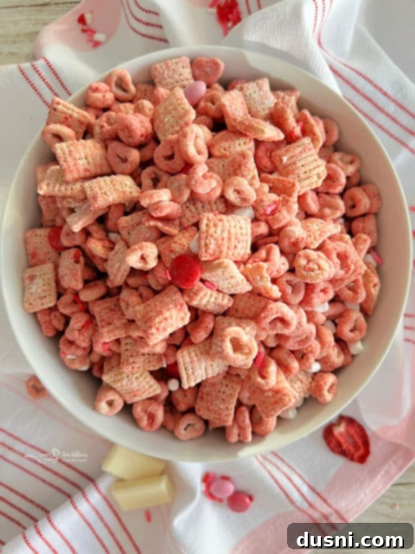 A bowl of crunchy pink puppy chow recipe, also known as muddy buddies, with a strawberry flavor, suitable for Valentine's Day or any sweet snack.