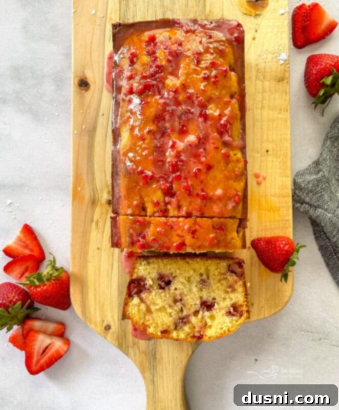 A beautiful loaf of Glazed Strawberry Bread, topped with a pink strawberry glaze, on a cooling rack.