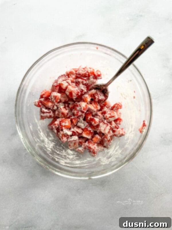 Diced fresh strawberries being coated with flour in a small bowl.