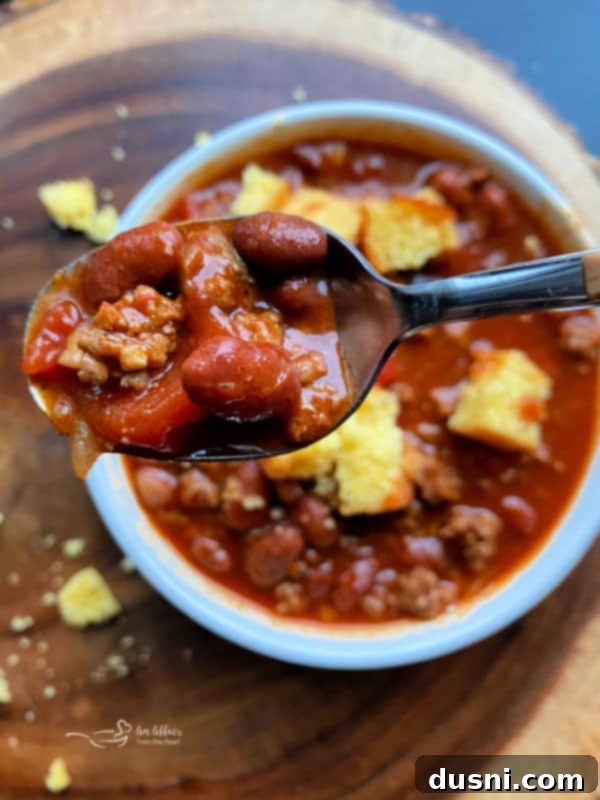 A close-up shot of a rustic wooden spoon scooping hearty Three Bean Chili from a large, deep pot, with steam rising, suggesting it's freshly cooked.