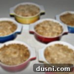 Six individual peach crisps on a wooden table, ready to be served.