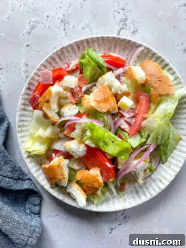 A large bowl of Little King Salad featuring layers of fresh lettuce, deli meats, cheese, tomatoes, and red onion, topped with dressing.