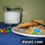 Side view of a few rainbow cookies on a white plate and a glass of milk on a table