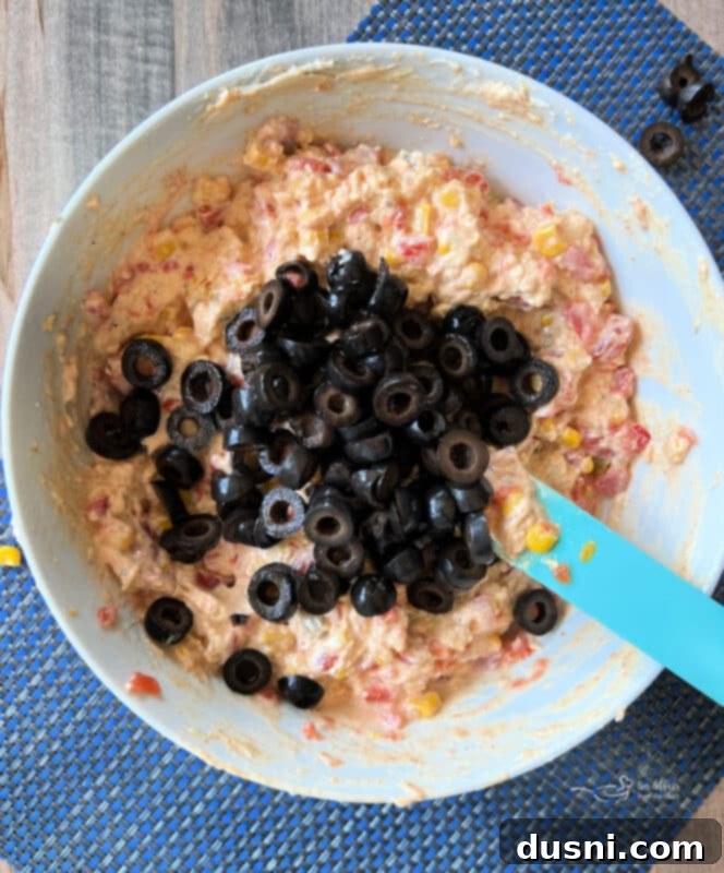 Easy 5 Ingredient Fiesta Corn Dip 8 Step three: Folding in sliced black olives into the corn dip mixture.