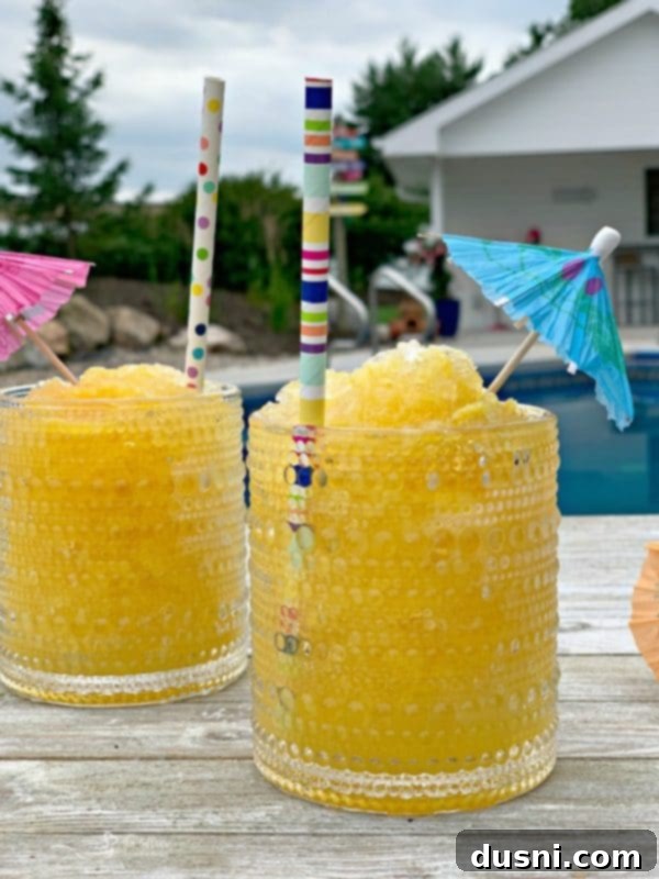 A glass of frozen vodka slush garnished with an orange slice and a straw, set against a summer backdrop.