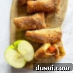 Air Fried Apple Pie Egg Rolls 18 Air Fryer Apple Pie Egg Rolls and half an apple on a wood board