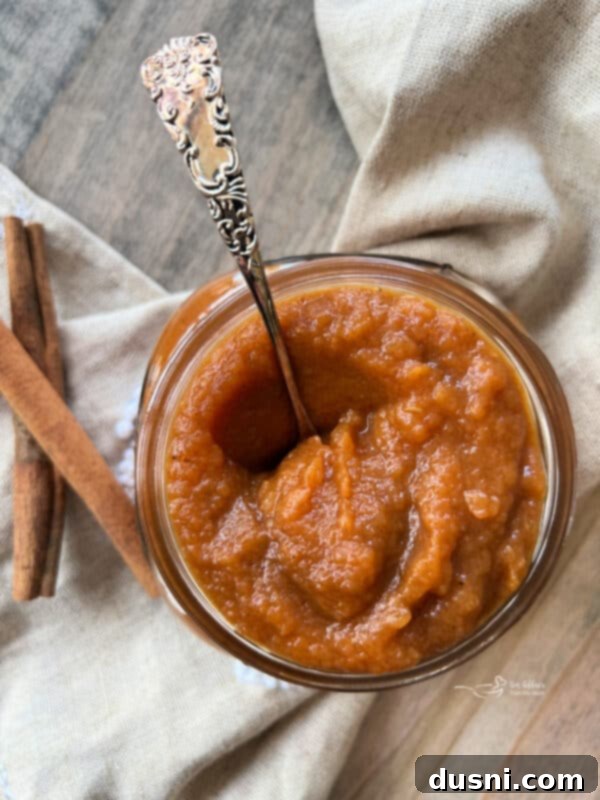 A close-up shot of Instant Pot Pumpkin Applesauce in a glass jar, garnished with a fresh apple slice.