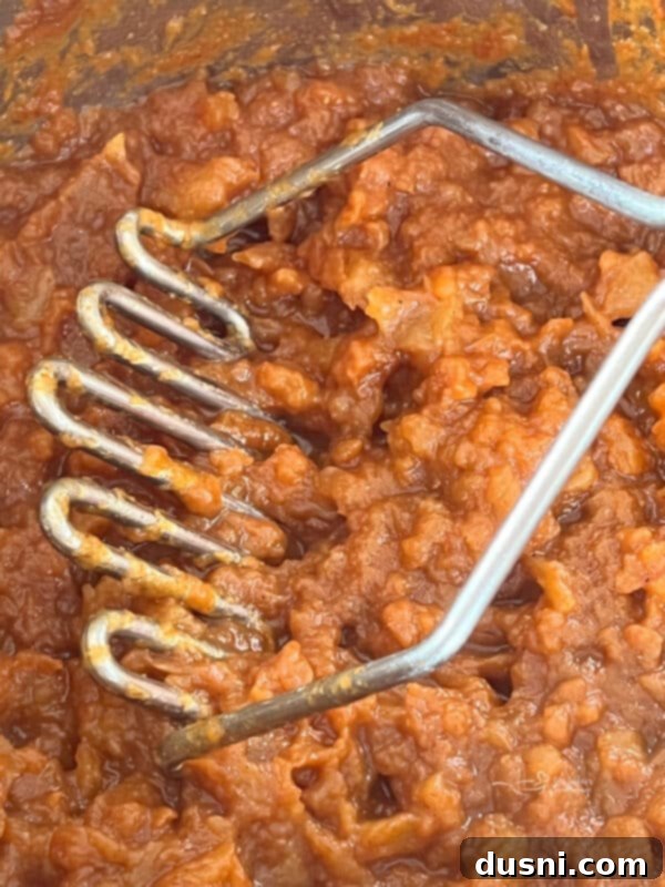 Step five of making Instant Pot Pumpkin Applesauce: Mashing the cooked apples in the Instant Pot.